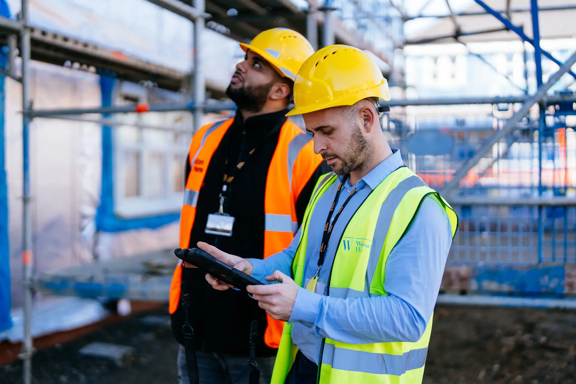 Two male staff members wearing hardhats on a construction site.