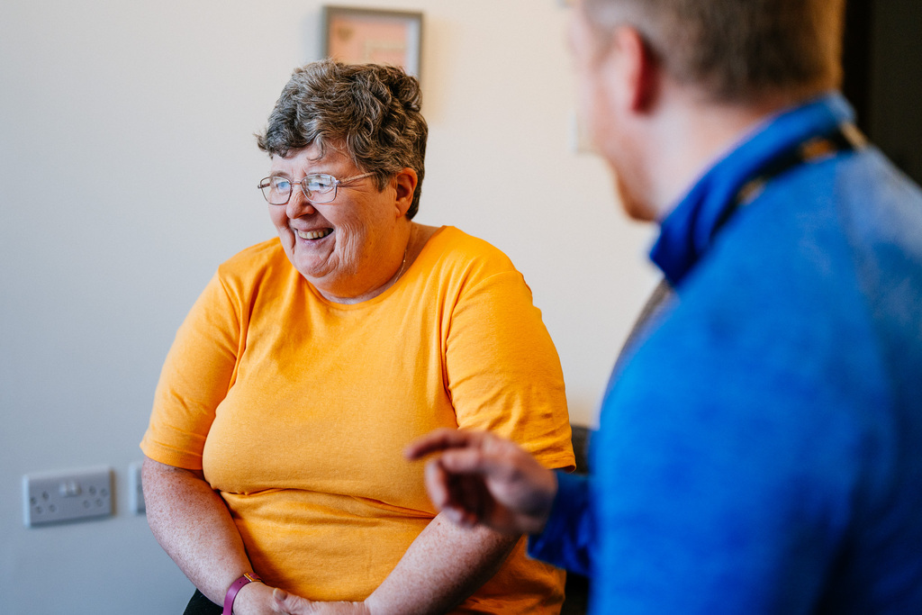 Woman in an orange t-shirt talking to a Be One Homes colleague.