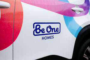 The Be One Homes logo on the side of a vehicle. The multicoloured brand thread is also visible.