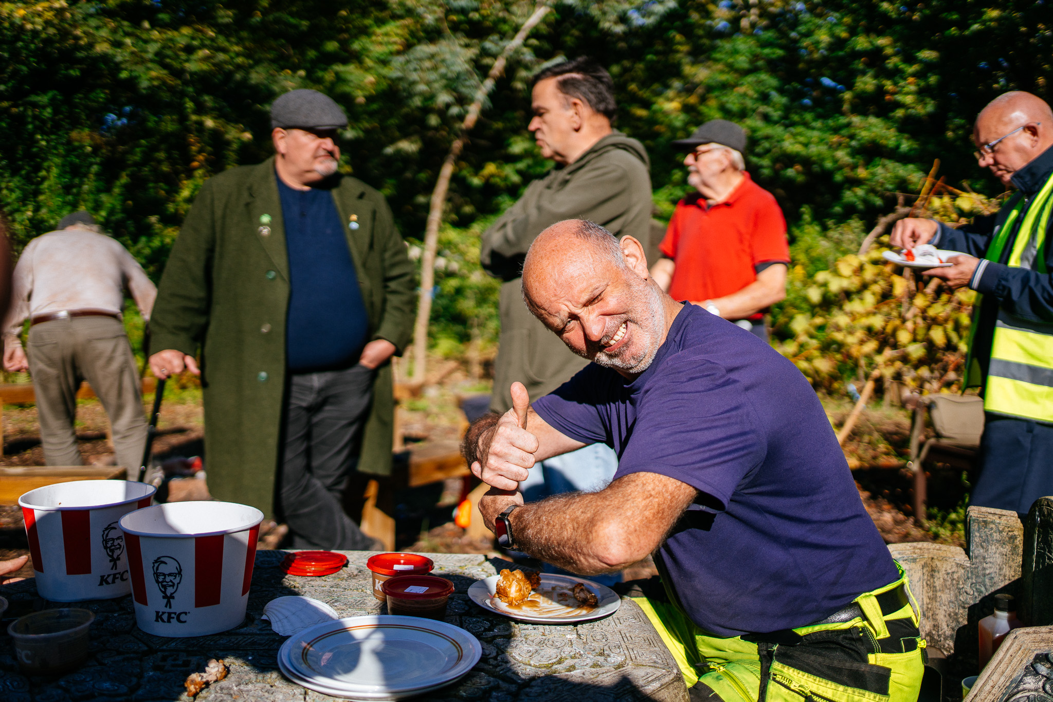 A man sits at a table at our Willow Hey Community Growing Project in Farnworth. It is sunny and he is giving a 'thumbs up' to the camera.