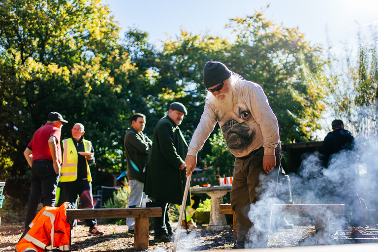 A man supervises a barbeque at our Willow Hey Community Growing Project in Farnworth. It is sunny and he is wearing a shirt with the face of a pug (dog) on it.