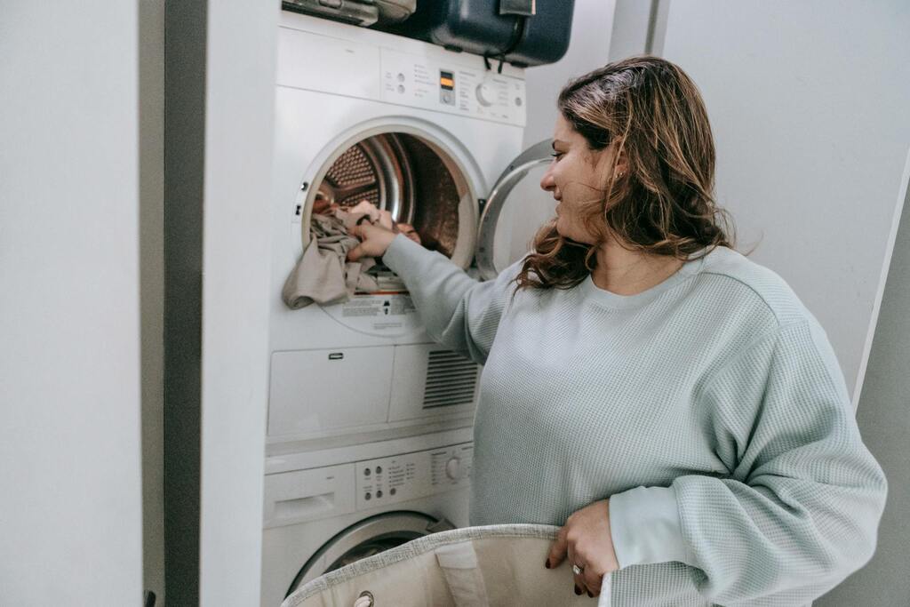 A lady smiling whilst loading clothes into a washing machine.