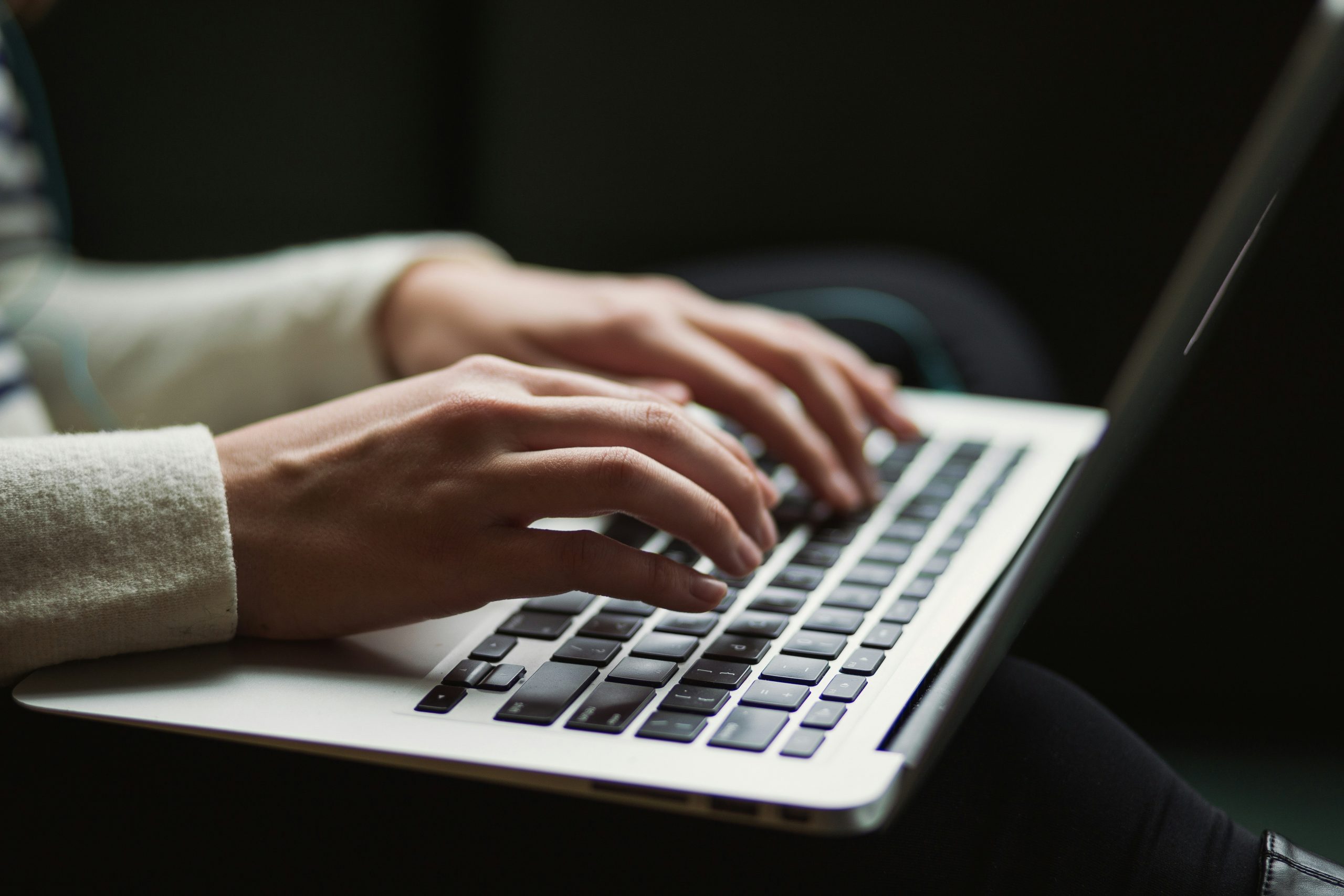 A person using a laptop. They have two hands on the keyboard whilst the laptop is placed on their lap.